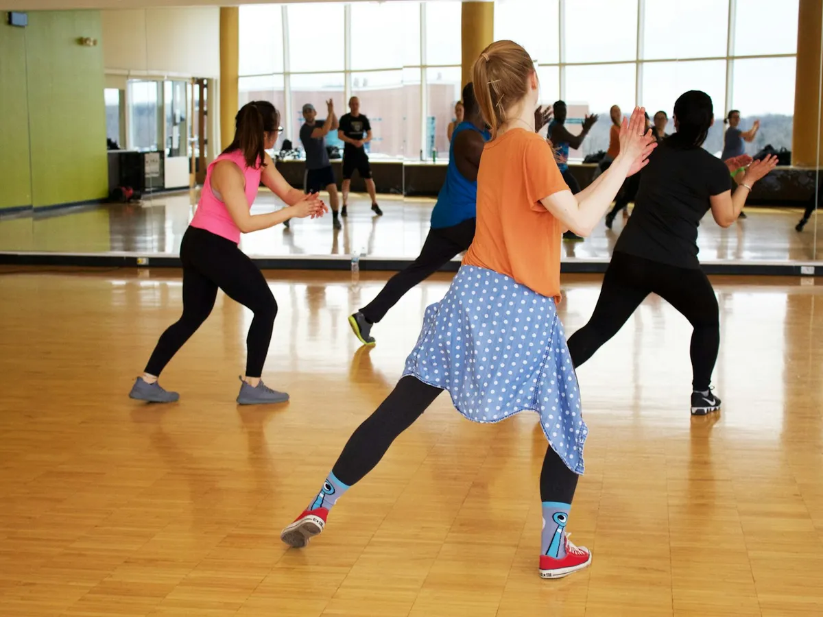 Turma dançando em uma sala com piso de madeira e espelhos
