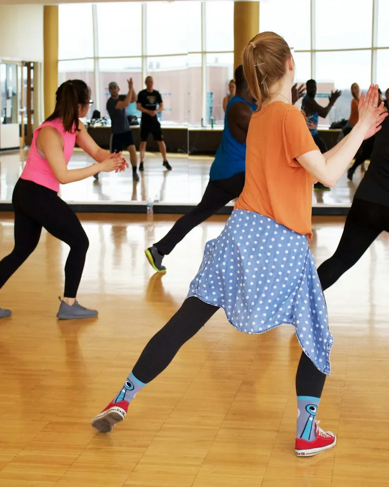 Turma dançando em uma sala com piso de madeira e espelhos