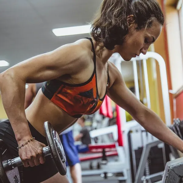 Camila Rocha, de top esportivo, fazendo remada com halter na academia