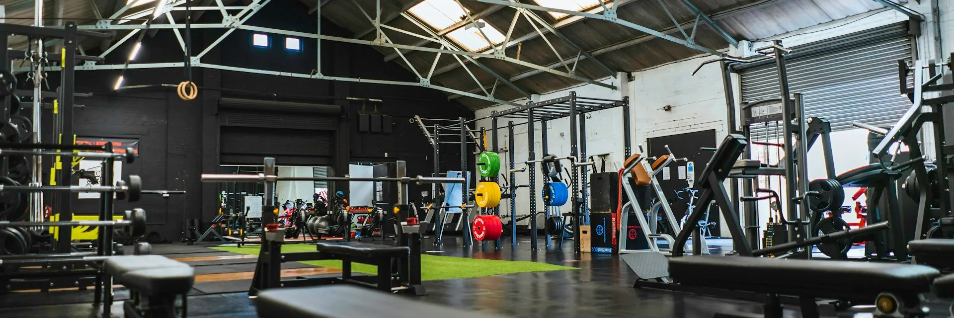Ampla área de treino com aparelhos, bancos e iluminação natural pelo teto